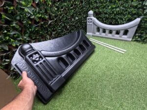 Hand holding the Regal Arch Concrete Mold with the finished concrete fence panel and two rebar-hole pipes in the background.